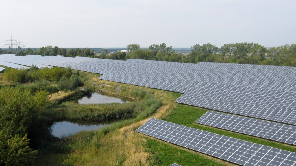 A large ground-mounted solar photovoltaic power plant in Saxony, Germany, with rows of solar panels stretching across an open landscape.
